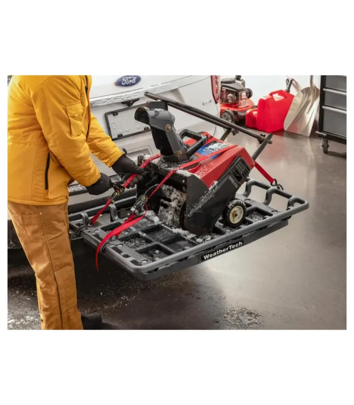 Hombre asegurando una barredora de nieve en el canasto de remolque WeatherTech, demostrando su uso para equipos pesados